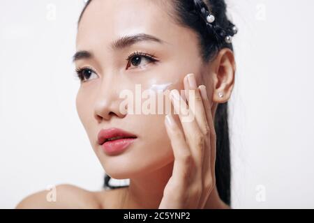 Beautiful young Vietnamese woman applying melting moisturizing and rejuvenating cream on her face Stock Photo