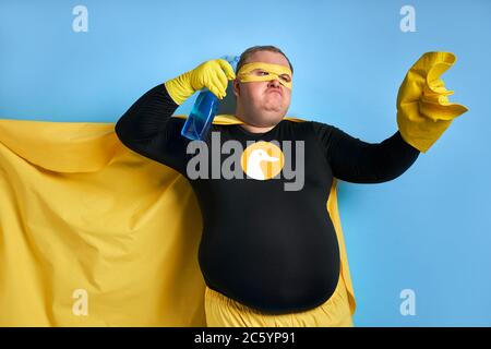 angry caucasian fat man in yellow costume applies detergent at rag, he is tired of dirt. cleaning concept Stock Photo