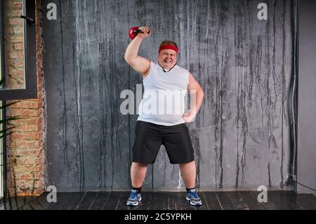 fat caucasian sporty man with weight for training in hands, man is engaged in fitness, isolated over gray background Stock Photo