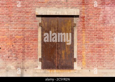 Old weathered rusty factory gate and the dated brown brick wall in the sunlight Stock Photo