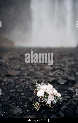 bridal bouquet of white roses, lily, burgundy cloves, brunia and leucadendron on the background of the waterfall in Iceland Stock Photo