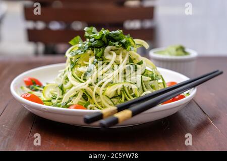 Noodles of spiralized zucchini, cucumber, cherry tomato, garlic in a creamy pesto from avocado. Raw food for vegetarian. Close up Stock Photo