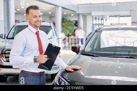 portrait of smiling car dealer at work, man in white formal shirt ready to talk about cars, automobiles and their chaacteristics to customers Stock Photo