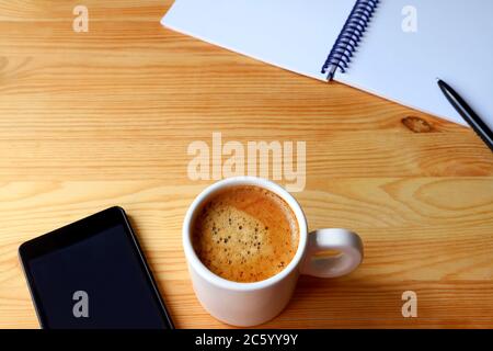 Cup of coffee with smartphone and notebook on wooden table for a concept of teleworking Stock Photo