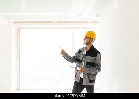 Thoughtful engineer in work clothes and yellow hardhat holding p Stock Photo
