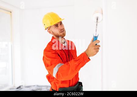 Thoughtful foreman in work clothes and yellow hardhat using pain Stock Photo