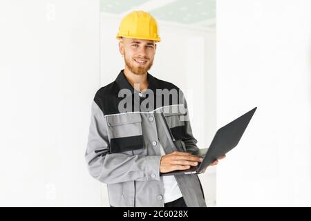 Young smiling engineer in work clothes and yellow hardhat joyful Stock Photo