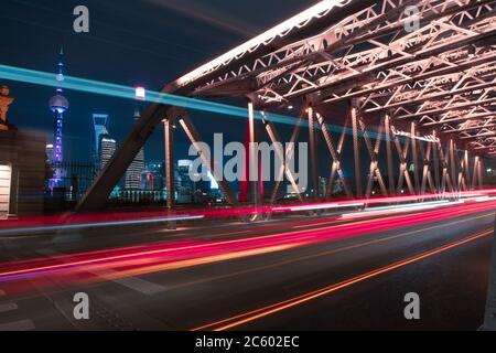 Night view of Waibaidu Bridge, a landmark steel bridge in Shanghai, with traffic and modern skyscrapers in the back.