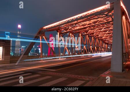 Night view of Waibaidu Bridge, a landmark steel bridge in Shanghai, with traffic and modern skyscrapers in the back.