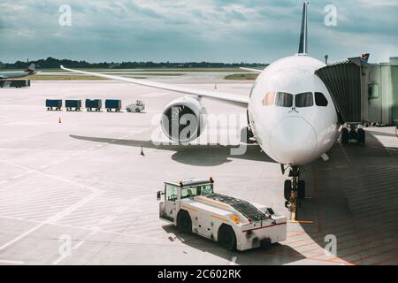 Aircraft Plane Boarding Passengers In Airport Terminal. Aircraft Tow Tractor And Fright Forklift Near Plane.