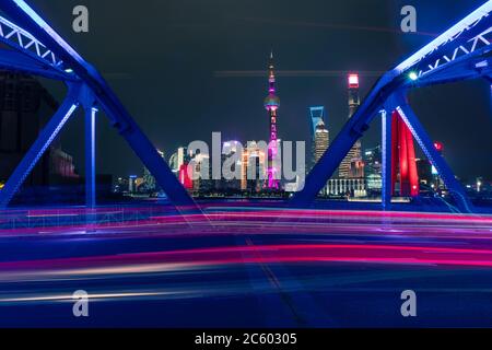 Night view of Waibaidu Bridge, a landmark steel bridge in Shanghai, with traffic and modern skyscrapers in the back.