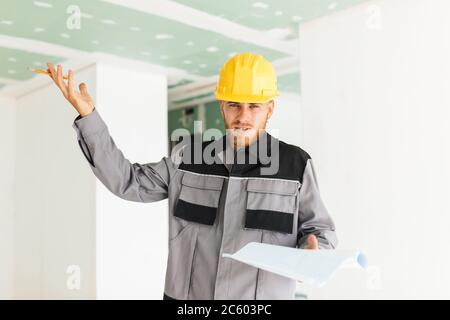 Young emotional engineer in work clothes and yellow hardhat hold Stock Photo