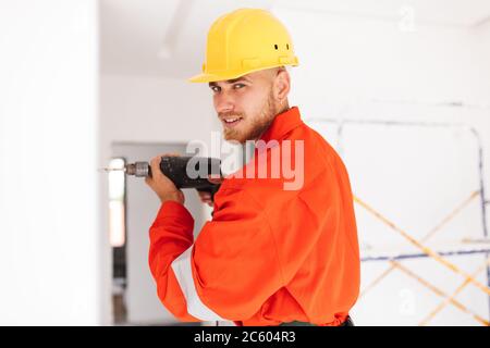 Young foreman in orange work clothes and yellow hardhat dreamily Stock Photo