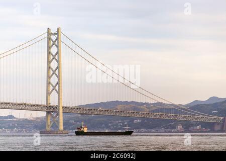 Cargo ship cruising under suspension bridge at sunset Stock Photo