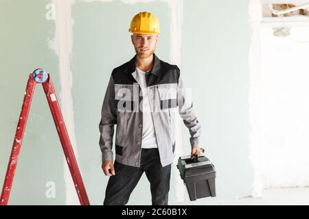 Young smiling engineer in work clothes and yellow hardhat holdin Stock Photo