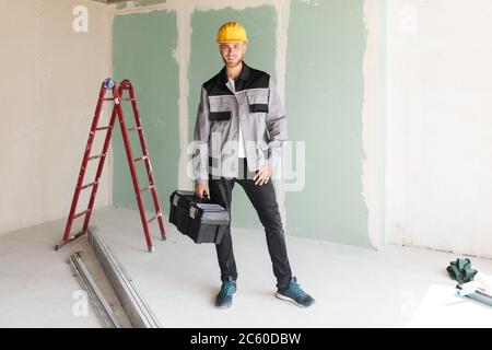 Smiling engineer in work clothes and yellow hardhat holding tool Stock Photo