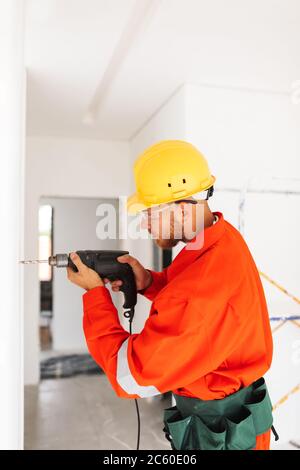 Young builder in orange work clothes and yellow hardhat using el Stock Photo
