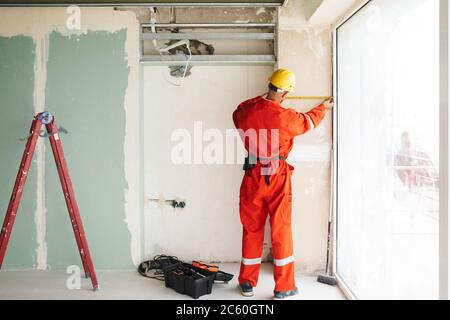Builder in orange work clothes and hardhat using measuring tape Stock Photo