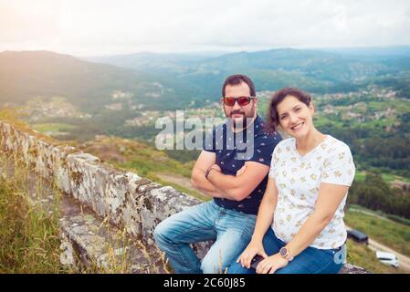 Pregnant heterosexual couple posing in front of a beautiful landscape with mountains and forests Stock Photo