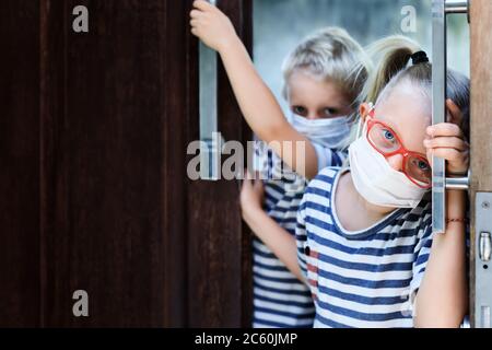 Little children looking unhappy and depressed after staying at home due banned street activity. Kids wearing medical face masks go out for outside wal Stock Photo