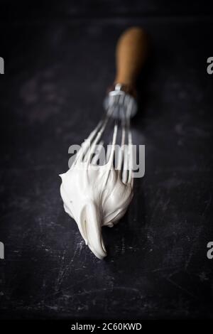 Hand balloon whisk with beaten egg white meringue mix. Closeup on black background. Stock Photo
