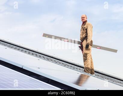 Solar panel energy. Portret of caucasian man electrical engineer working in solar station on roof against blue sky. Development sun alternative energy Stock Photo