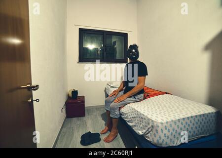 man sitting on the bed wearing a scary mask Stock Photo