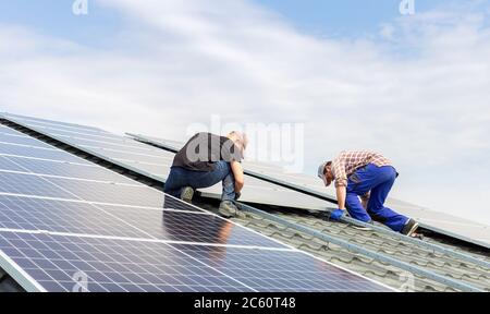 Electrical engineers mans are working installing solar panels on solar station on house roof against blue sky. Building a solar station. Alternative Stock Photo