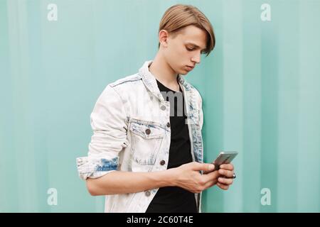 Portrait of young thoughtful man standing and using his cellphone on over blue background Stock Photo