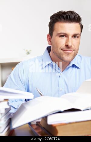 Young smiling man in the office is learning between piles of books Stock Photo