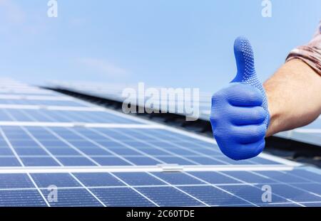 Male worker showing thumbs up, positive gesture against solar panel, solar station. Like to alternative energy sun energy power. Man installing solar Stock Photo
