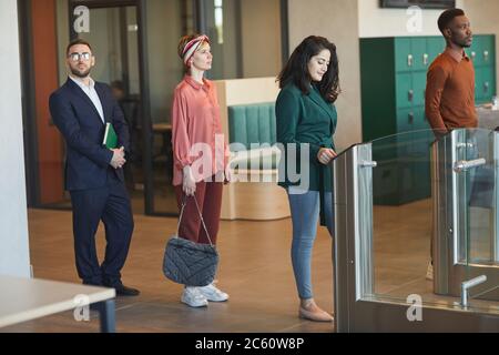 Side view at multi-ethnic group of people standing in line while passing automated gate to enter office building, focus on young Middle-Eastern woman Stock Photo