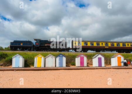 Goodrington Sands, Paignton, Devon, UK.  6th July 2020.  The Dartmouth Steam Railway reopens with a passenger train hauled by 7827 Lydham Manor passing behind the beach huts at Goodrington Sands on its trip to Kingswear after leaving the station at Paignton in Devon after the further easing of coronavirus lockdown rules allowed the heritage line to carry passengers again.  Picture Credit: Graham Hunt/Alamy Live News
