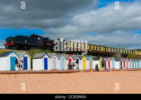 Goodrington Sands, Paignton, Devon, UK.  6th July 2020.  The Dartmouth Steam Railway reopens with a passenger train hauled by 7827 Lydham Manor passing behind the beach huts at Goodrington Sands on its trip to Kingswear after leaving the station at Paignton in Devon after the further easing of coronavirus lockdown rules allowed the heritage line to carry passengers again.  Picture Credit: Graham Hunt/Alamy Live News Stock Photo