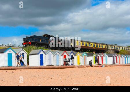 Goodrington Sands, Paignton, Devon, UK.  6th July 2020.  The Dartmouth Steam Railway reopens with a passenger train hauled by 7827 Lydham Manor passing behind the beach huts at Goodrington Sands on its trip to Kingswear after leaving the station at Paignton in Devon after the further easing of coronavirus lockdown rules allowed the heritage line to carry passengers again.  Picture Credit: Graham Hunt/Alamy Live News Stock Photo