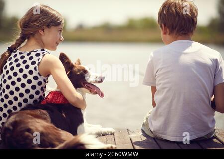 Little boy and girl with dog sitting on a wood pier and fishing in a pond.