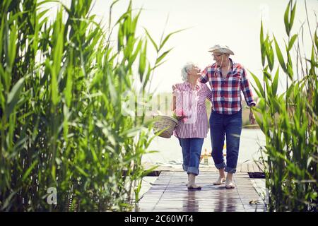 Smiling elderly man and woman at river enjoying together on romantic picnic. Stock Photo