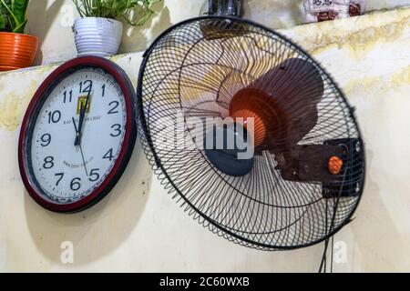 HANOI, VIETNAM, APR 20 2019, clock hangs on the wall next to a rotating fan at coffee shop Stock Photo