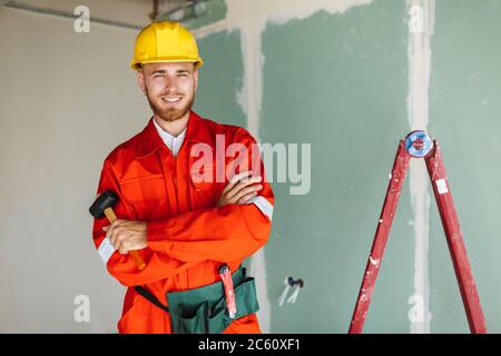 Smiling builder in orange work clothes and hardhat holding hamme Stock Photo