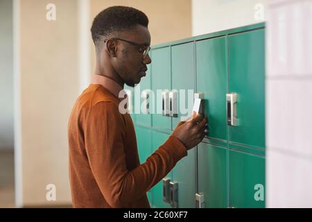 Side view portrait of young African-American man opening locker in college or office building, copy space Stock Photo