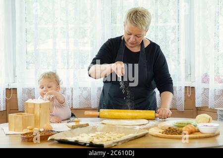 Happy grandmother and little helper knead dough bake cookies, child enjoy baking Stock Photo