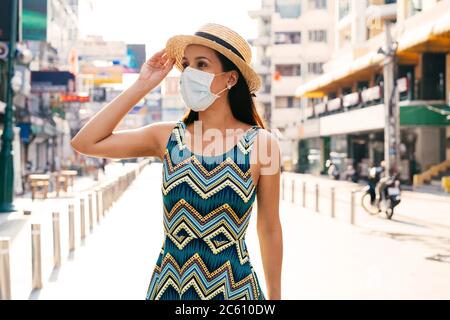 Portrait of young Mexican woman wearing face mask and hat in city looking away Stock Photo