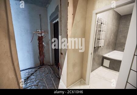 Horizontal image, view from the corridor to finished bathroom and to unfinished other room with heating pipe system on the floor. Concept of home renovation and refurbishment. Stock Photo