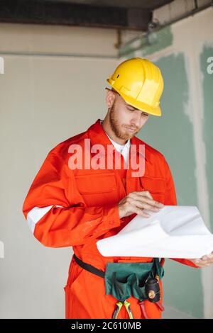 Young foreman in orange work clothes and yellow hardhat thoughtf Stock Photo