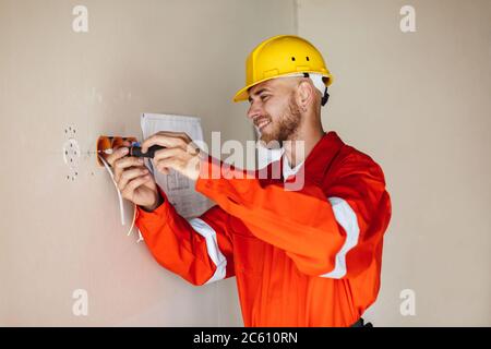 Smiling foreman in orange work clothes and yellow hardhat using Stock Photo