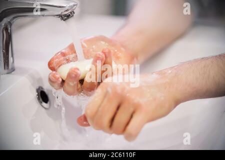 A person holds soap under the tap water and is going to wash his hands thoroughly over the sink. Hygiene. Clean. Stock Photo