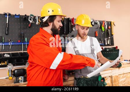 Two builders in work clothes and yellow hardhats thoughtfully lo Stock Photo