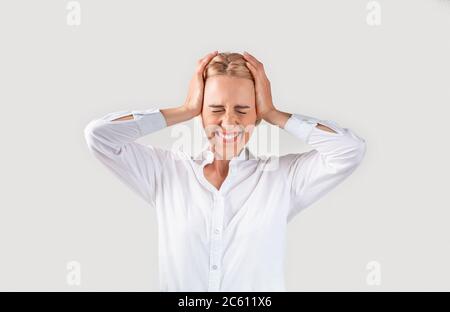 Emotional mature businesswoman holding her head in disbelief on light background Stock Photo
