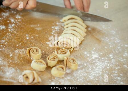 Close up female baker slices dough roll makes rolls with sugar cinnamon for buns Stock Photo