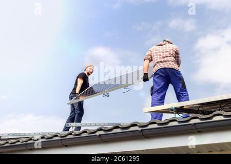 Electrical engineers mans are working installing solar panel on solar station on roof against blue sky. Development sun alternative energy technology Stock Photo